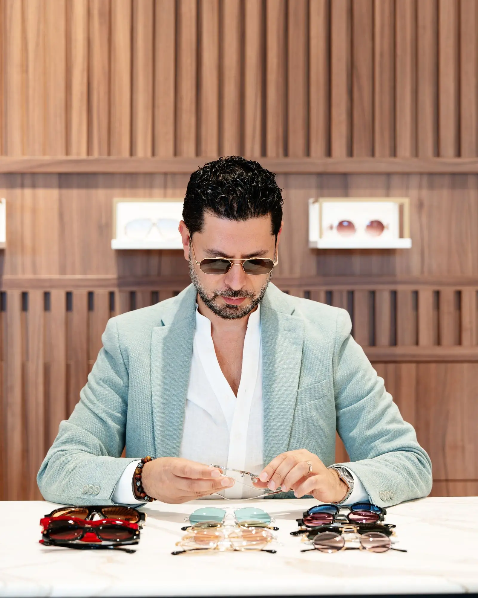 Edgar à la table de la boutique EDGAR Optique d’Uccle, devant le mur de bois
