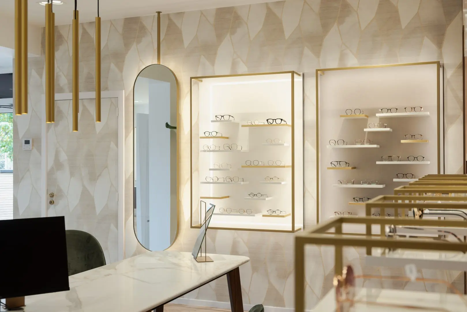 Miroir ovale suspendu et vitrines encadrées de laiton, sur un papier peint à motif de feuilles