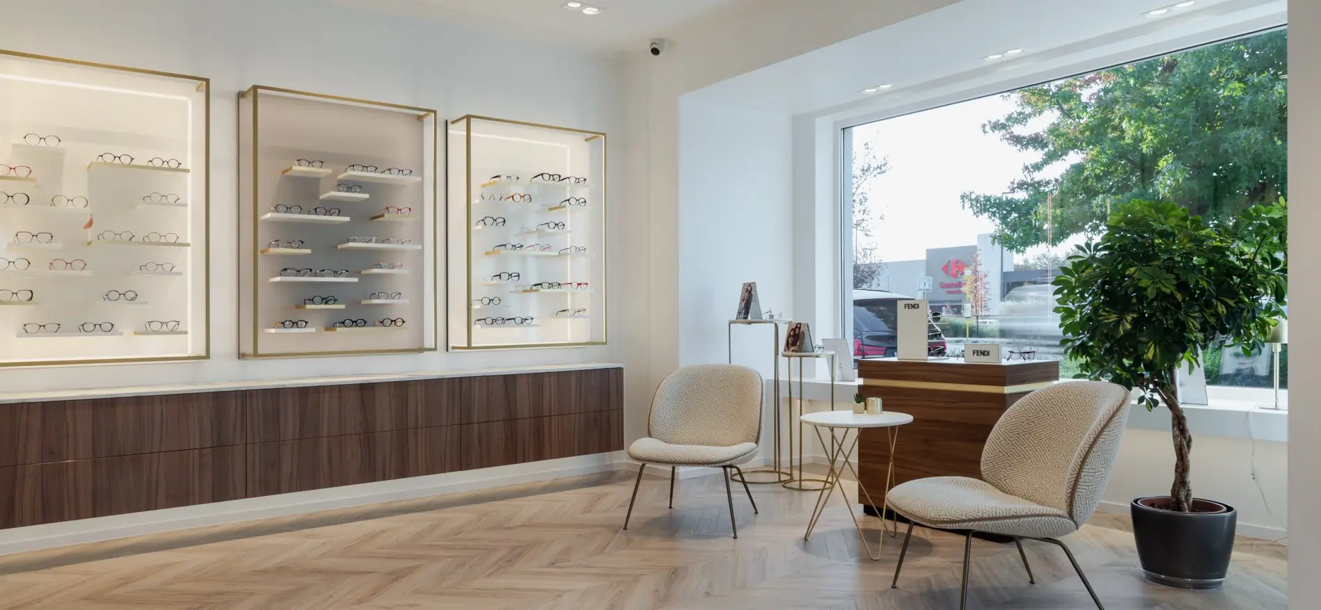 Coin salon avec deux fauteuils et une table d’appoint, face à la grande vitrine, vitrines de montures au mur