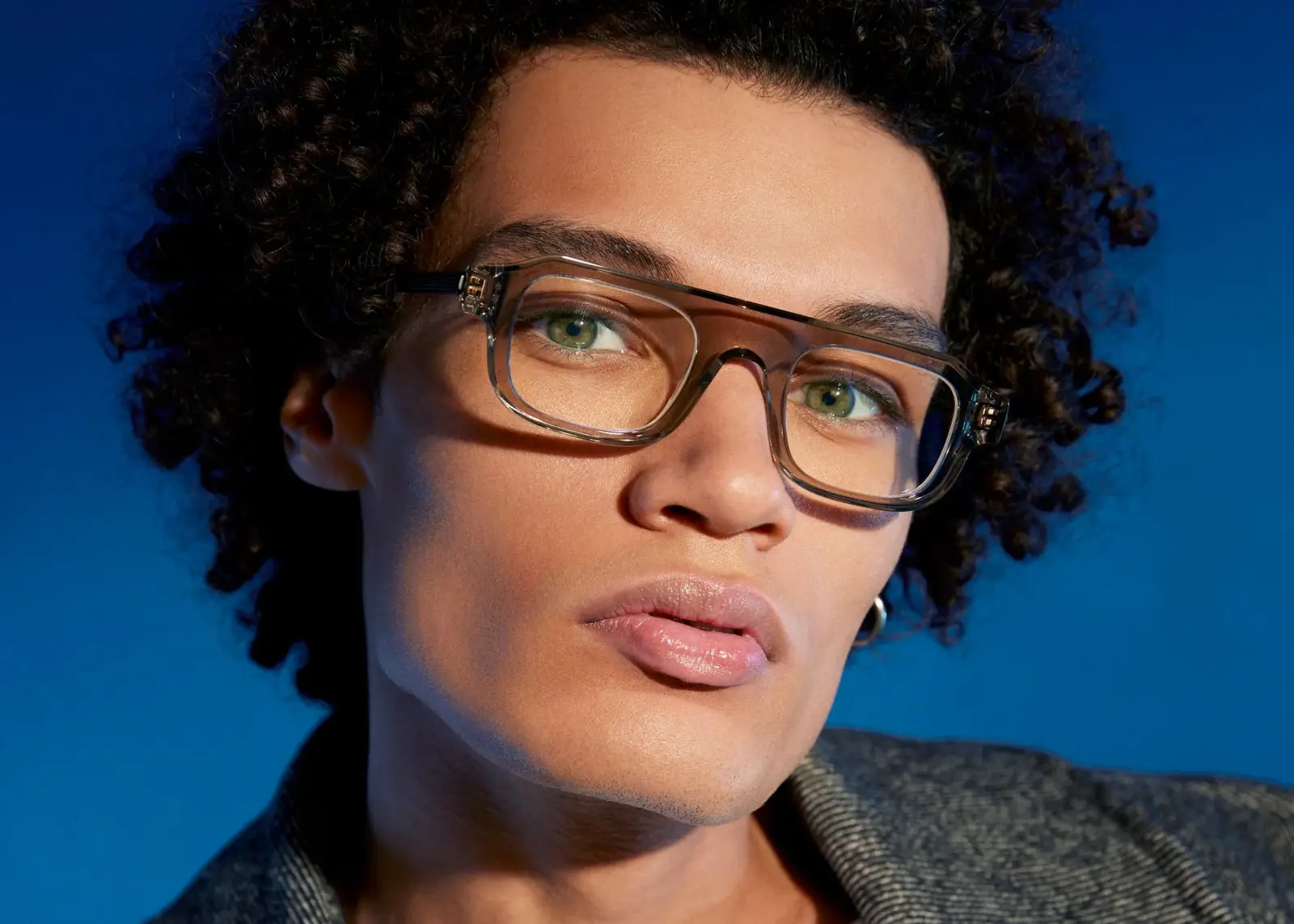 Homme aux cheveux bouclés portant des lunettes de vue Thierry Lasry translucides, sur fond bleu vif